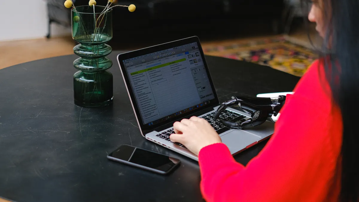 person typing on a laptop beside a robotic hand